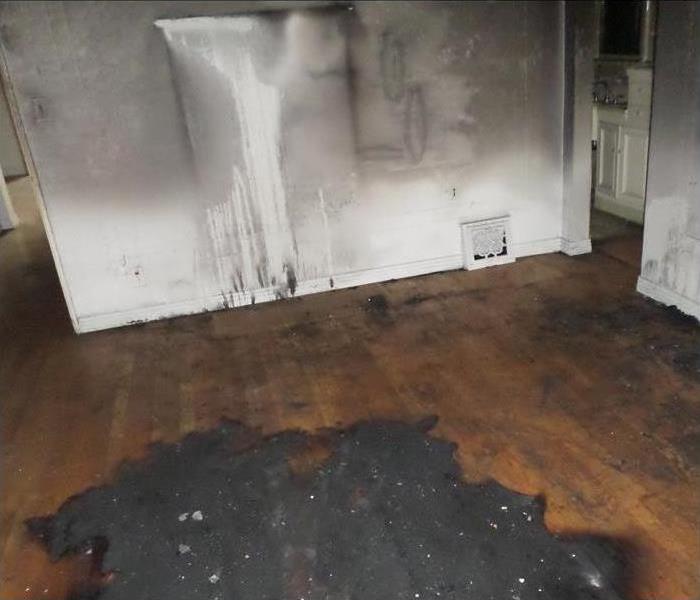 hardwood floor and white wall with black soot and damage